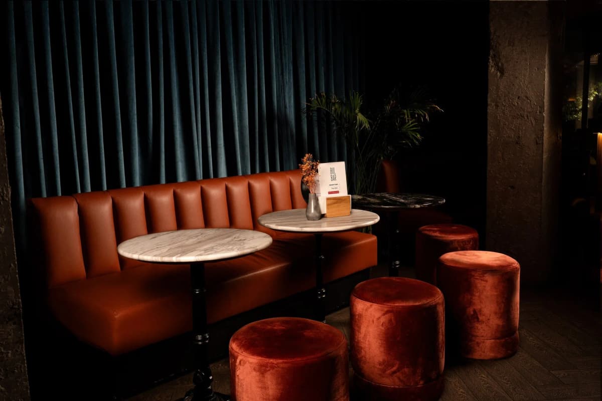 Marble tables and velvet pouffes along the leather banquette beside the curtain